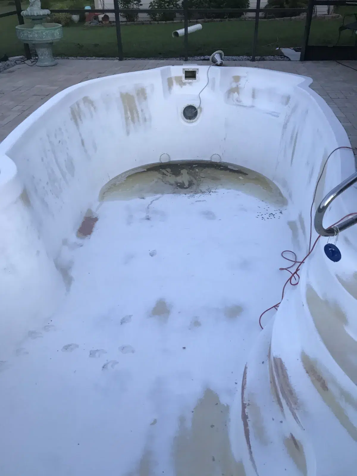 Drained fiberglass pool with a weathered white interior before resurfacing